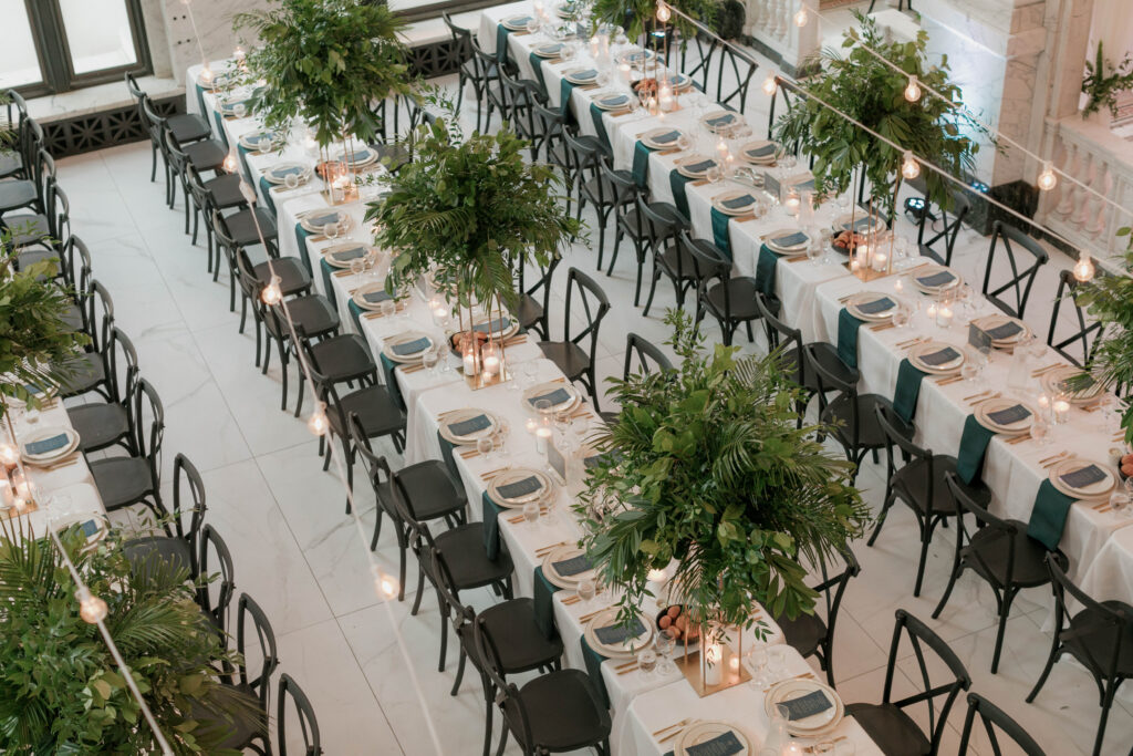 above view of long tables, with 15 chairs on each side, featuring tall greenery arrangements and low candle votives