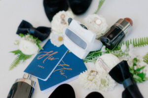 white surface featuring vow books, cologne, two bowties, flowers, two wedding bands and their custom viewfinder invitation.