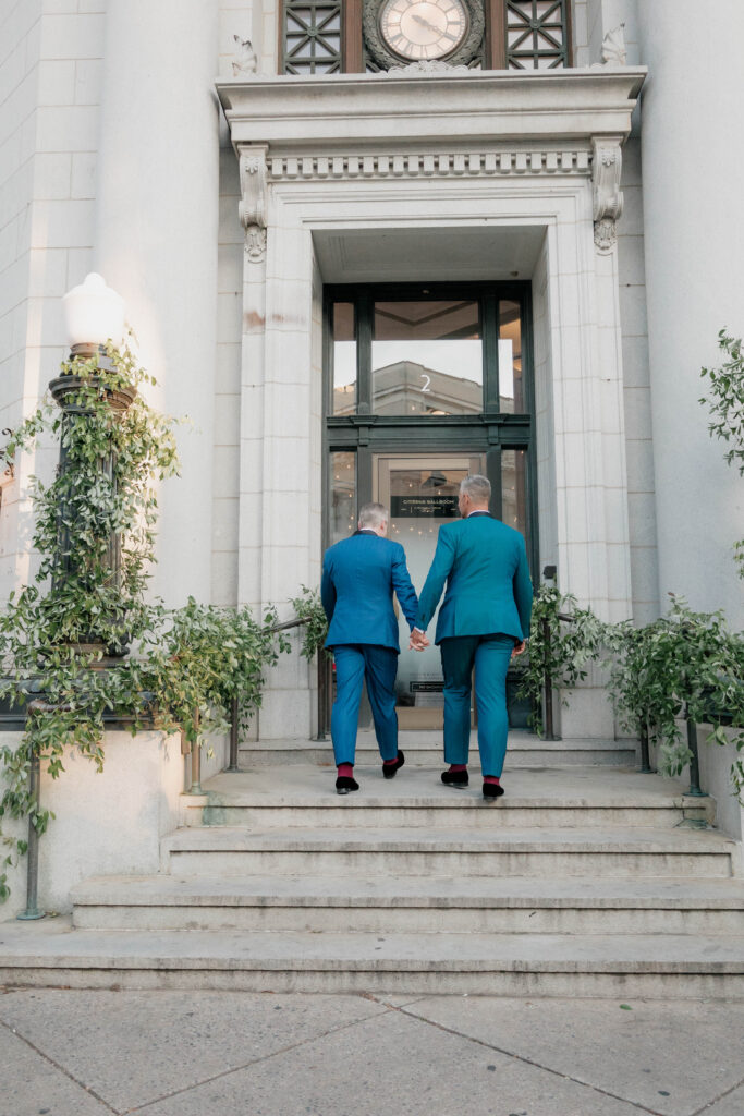 Two men in blue suits holding hands on steps.